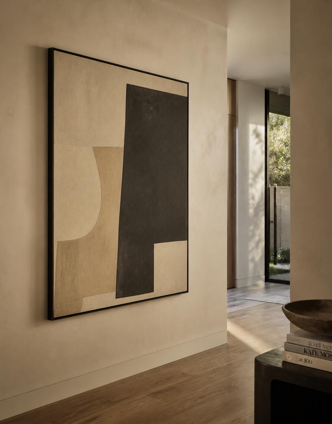Large abstract artwork in muted beige and charcoal tones on a warm plaster wall in a contemporary residential interior